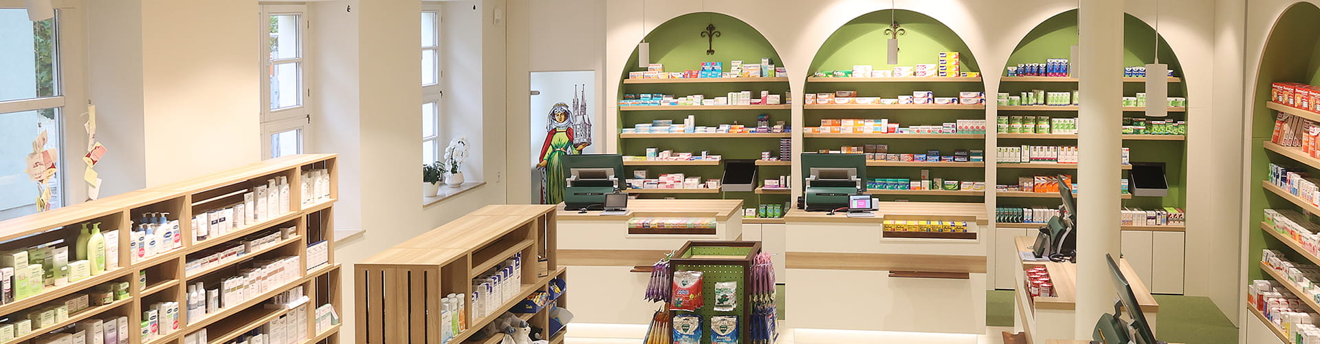 Elisabeth-Apotheke Freyburg Blick auf den Verkaufsraum mit Handverkaufsbereich, Kassenbereich mit vier Kassen & einer modernen Optik in Weiß- & Grüntönen in Kombinationen mit Holz