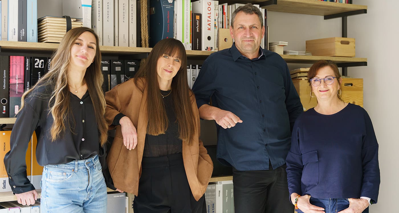mediraum design Teamfoto Karyna Stopicheva, Elisa Borchert, Hagen Brockhaus & Kerstin Hornig stehen leicht lächelnd vor einem Regal mit vielen Büchern & Holzkisten